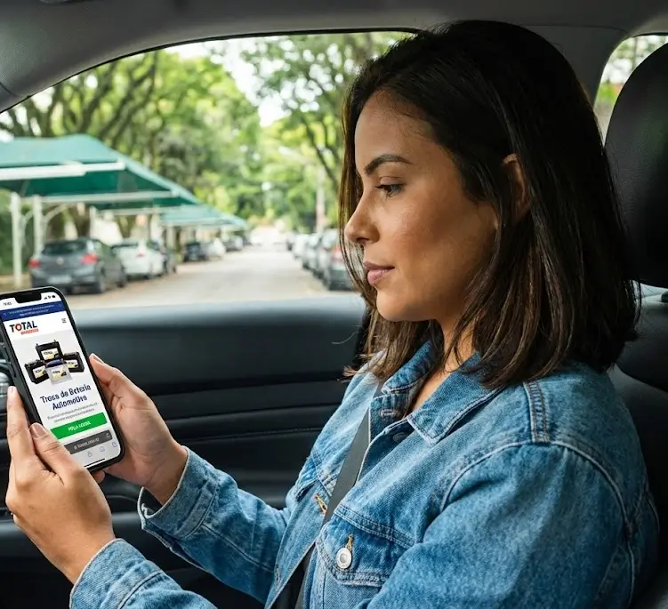 Mulher olhando celular no site da Total Baterias parada no carro em uma rua arborizada
